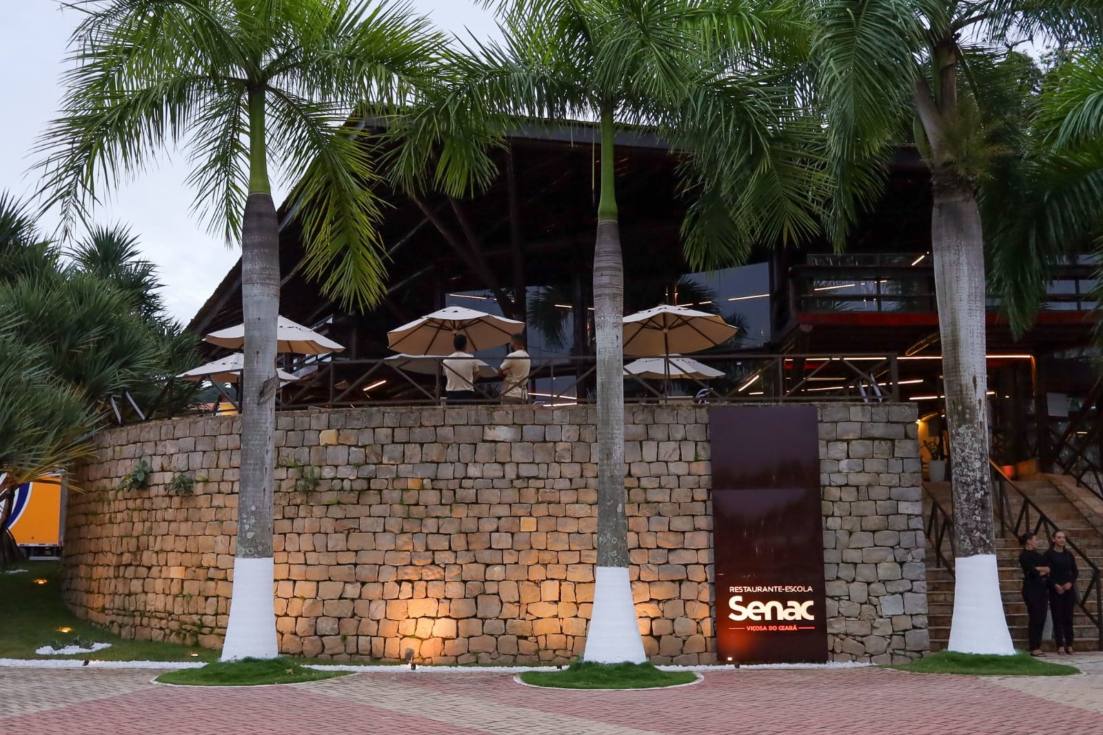 Fachada do Restaurante-Escola Senac em Viçosa do Ceará, na região da Ibiapaba, com área externa e muro de pedra ao entardecer.